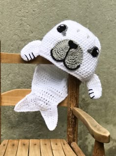 a crocheted stuffed seal sitting on top of a wooden chair next to a wall