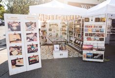 an outdoor book stand with several books on it's sides and two white tables in the background