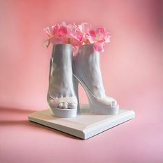 a pair of white high heeled shoes with pink flowers in them on a platform