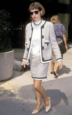 a woman walking down the street wearing sunglasses and a suit with a white shirt underneath