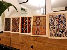 four framed rugs sitting on top of a wooden dresser next to a plant and mirror