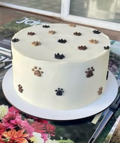 a white cake with paw prints on it sitting on a table next to a magazine