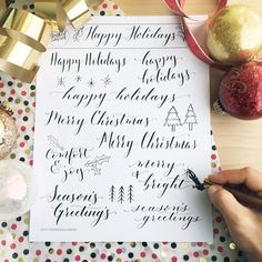 a person writing on a sheet of paper next to christmas decorations and presents, with the words happy holidays written in cursive