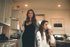 two women standing in a kitchen drinking from cups