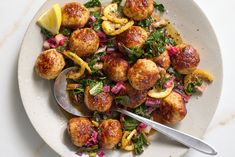 a white plate topped with meatballs and veggies next to a lemon wedge