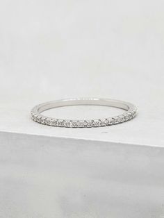 a white gold wedding band with round diamonds on top of a block of concrete in front of a plain background