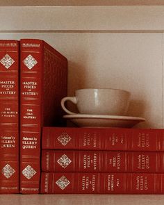 a stack of red books sitting on top of a shelf next to a cup and saucer