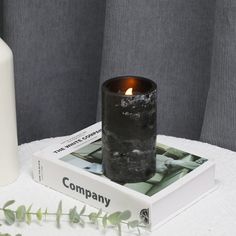 a candle sitting on top of a book next to a white vase and green plant