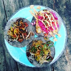 three tortillas on a blue plate topped with slaw and toppings sitting on a wooden table