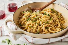 a pan filled with pasta and parsley on top of a table next to wine glasses