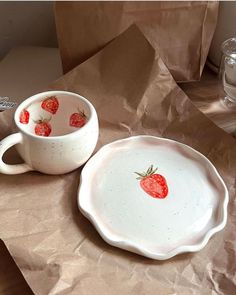 two bowls with strawberries painted on them sitting on a table next to brown paper