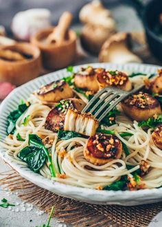 a plate of pasta with seared scallops and spinach garnish