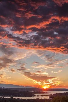 the sun is setting over some water and hills