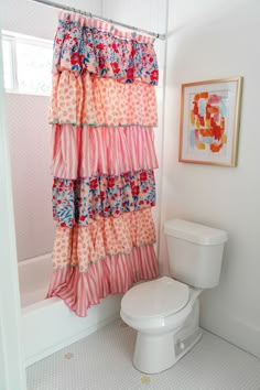 a white toilet sitting next to a bath tub under a window covered in colorful shower curtains