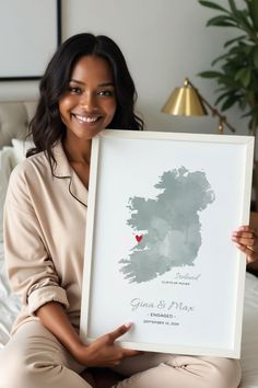 a woman sitting on a bed holding up a framed poster with the map of ireland