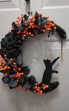 a black cat sitting on top of a door next to an orange and black wreath