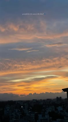 the sky is filled with clouds as the sun sets in the distance behind some buildings