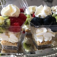 desserts are arranged in small clear containers on a silver platter with fruit and whipped cream