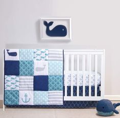 a baby's room with blue and white quilts, crib, whale wall decor