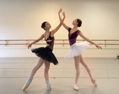 two young ballerinas are dancing in an empty room with their arms up to each other