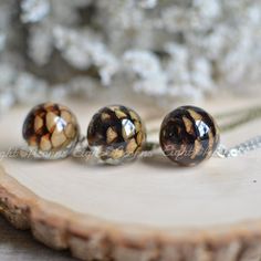 three glass beads sitting on top of a piece of wood next to a silver chain