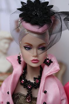 a doll wearing a pink coat and hat with black flowers on it's head