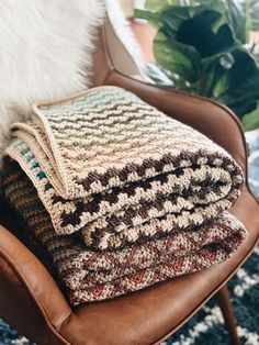 a pile of blankets sitting on top of a brown chair next to a potted plant