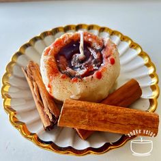 cinnamon rolls on a white and gold plate with cinnamon sticks next to them, along with an orange stick