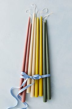 six candles tied together with blue ribbon on white background, one is yellow and the other two are pink