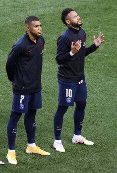 two soccer players stand on the field and applaud with their hands in front of them