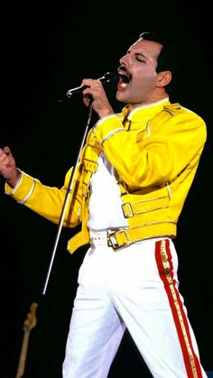 a man in yellow jacket and white pants holding a microphone while singing into a mic