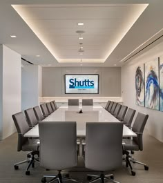 an office meeting room with large white table and grey chairs in front of the screen that says shuts