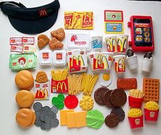 a table topped with lots of toy food and toys like chips, hamburgers, hotdogs, macaroni and cheese