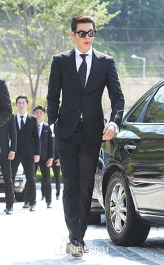 a man in a suit and sunglasses walking down the street with other men behind him