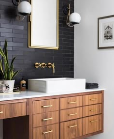 a bathroom with black brick walls and gold trim on the mirror above the double sink