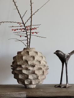 a bird statue next to a vase with berries on it and a tree branch in the background