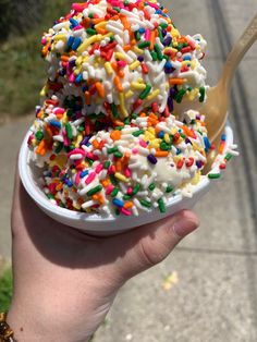 a hand holding a bowl filled with sprinkles and ice cream on top of a sidewalk