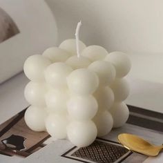 a white candle sitting on top of a table next to a gold spoon and mirror