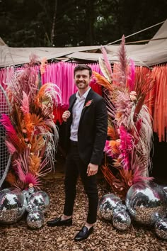 a man in a suit standing next to some silver balls and pink feathers on the ground