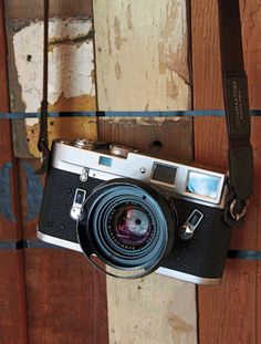 an old camera hanging on the side of a wooden wall with a strap around it