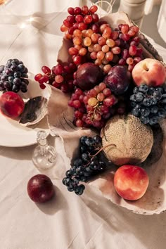 a bowl filled with lots of fruit sitting on top of a white tablecloth covered table