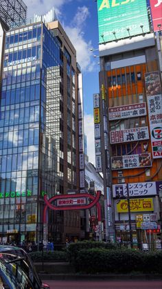 cars are driving down the street in front of tall buildings with advertisements on them and people walking by