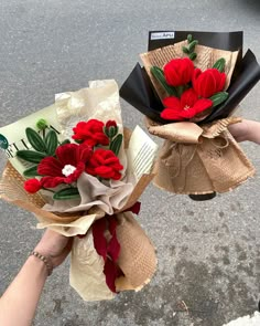 two bouquets of flowers are being held by someone's hand on the street