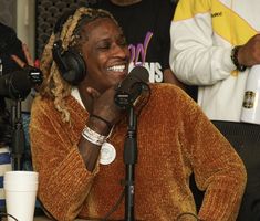 a woman sitting in front of a microphone with headphones around her neck and smiling