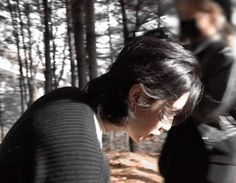 a woman standing in the woods looking down at something