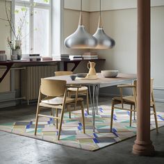 three hanging lights over a table in a room with chairs and a vase on it