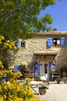 a stone house with blue shutters and yellow flowers