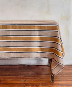 a striped tablecloth on a wooden bench in front of a white wall and wood floor