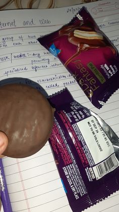 a hand holding a chocolate covered doughnut next to some writing paper and candy bars