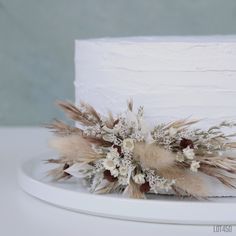 a wedding cake decorated with dried flowers and feathers